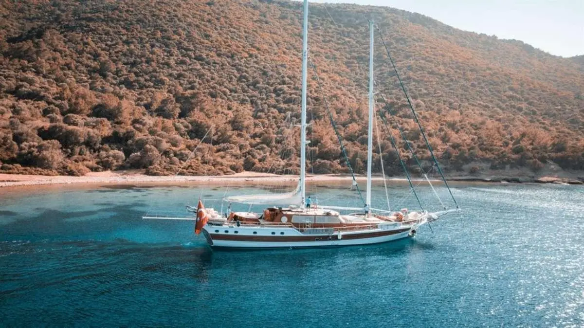 Sailing yacht Wicked Felina anchored in blue water with hills in background