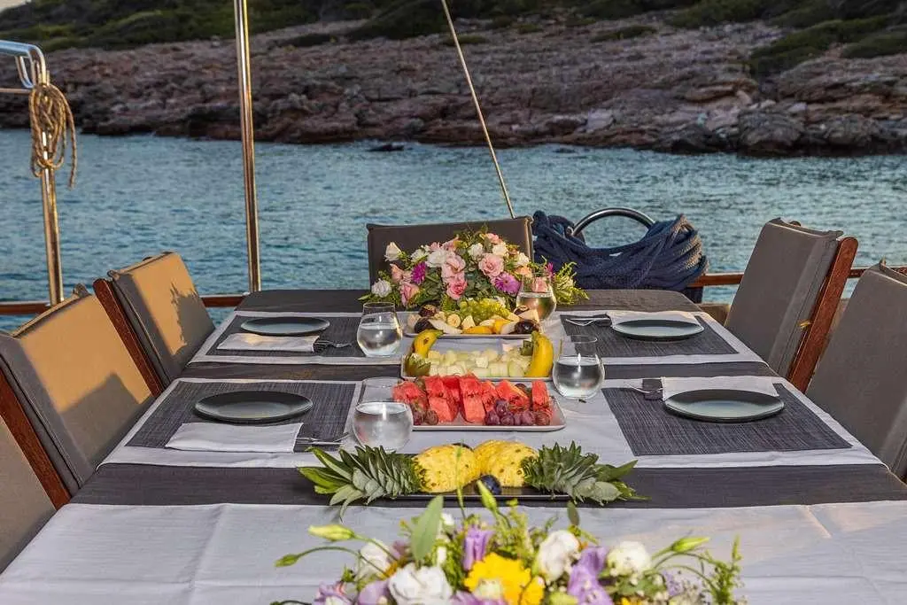Elegant yacht dining table set with fresh fruit and flowers, overlooking turquoise sea.