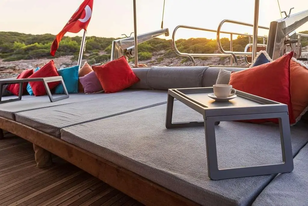 Yacht Bodrum Queen deck seating with low table and red cushions by water