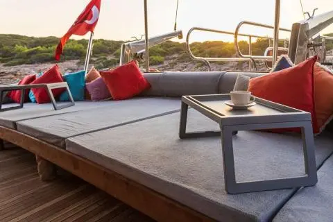 Yacht Bodrum Queen deck seating with low table and red cushions by water