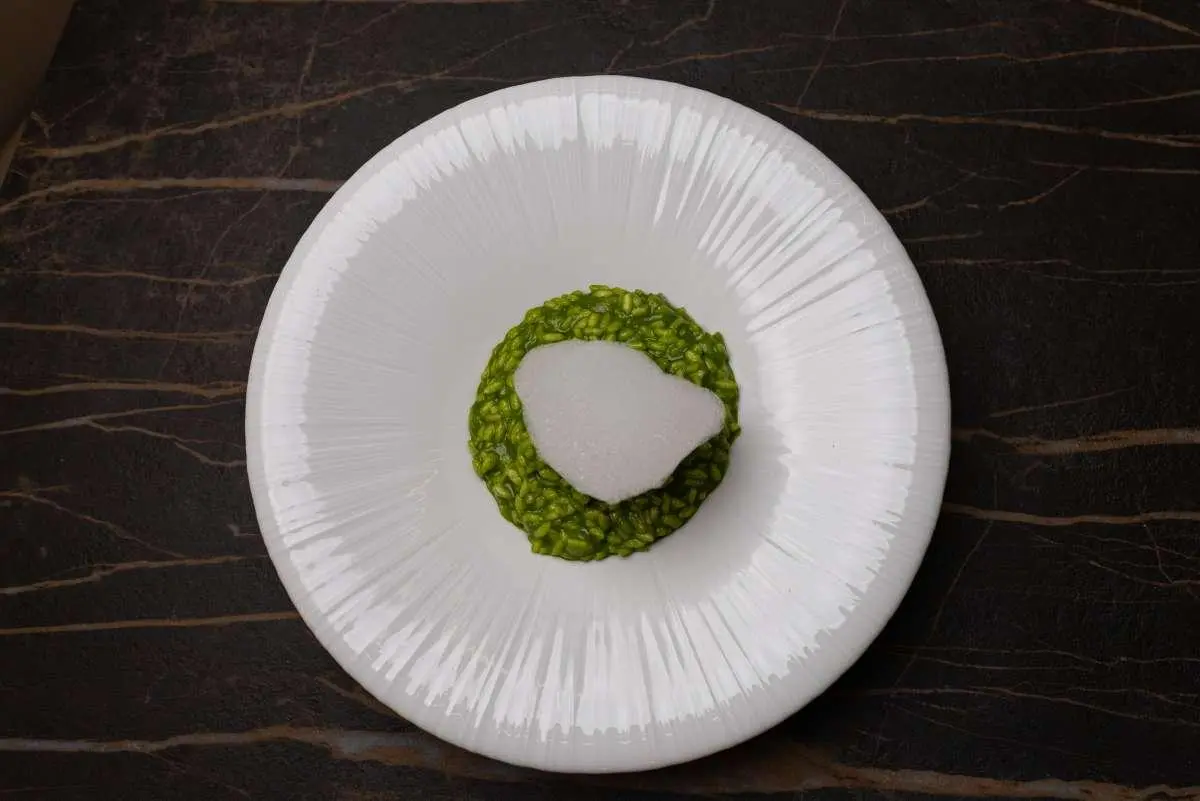 Green risotto with a white heart-shaped garnish on a white textured plate