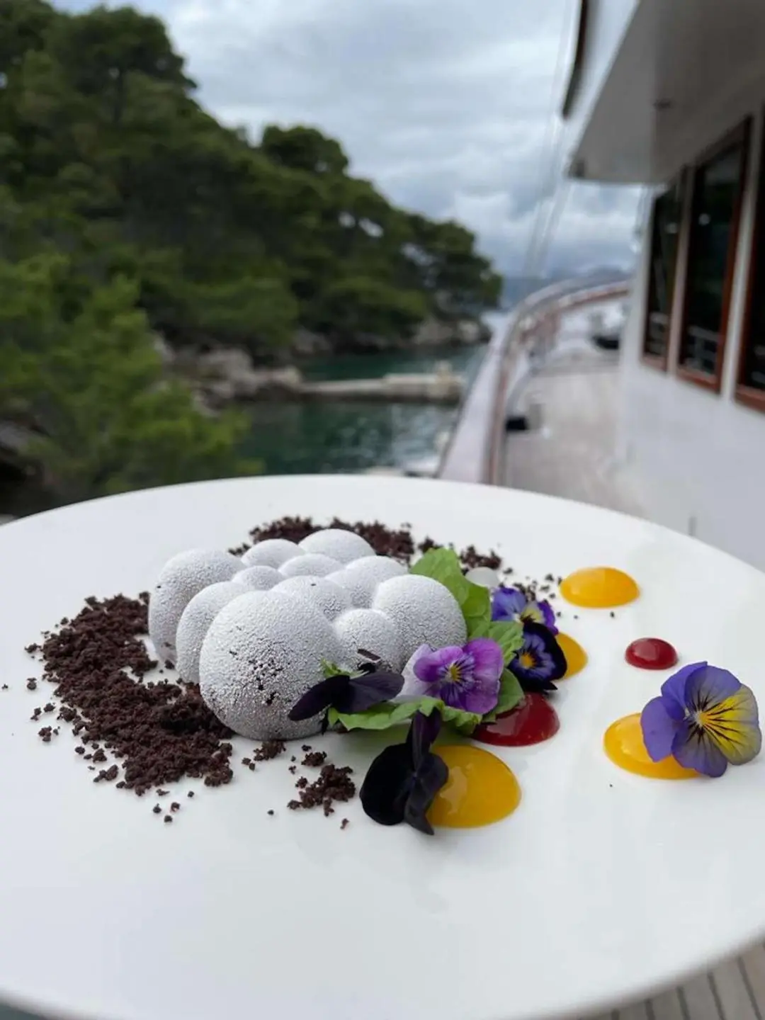 Corsario yacht deck scene with a white plated dessert, flowers, and purple petals