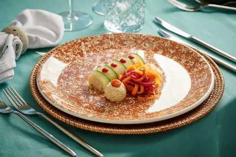 Elegant plated dish on a turquoise table with gold-rimmed plate and cutlery