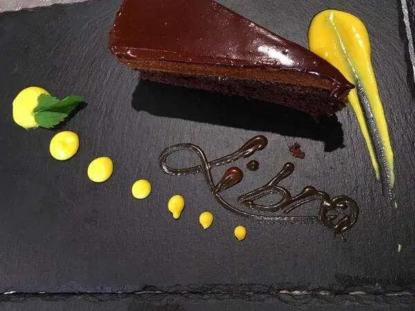 Chocolate ganache cake slice with decorative sauces and mint leaf on slate plate