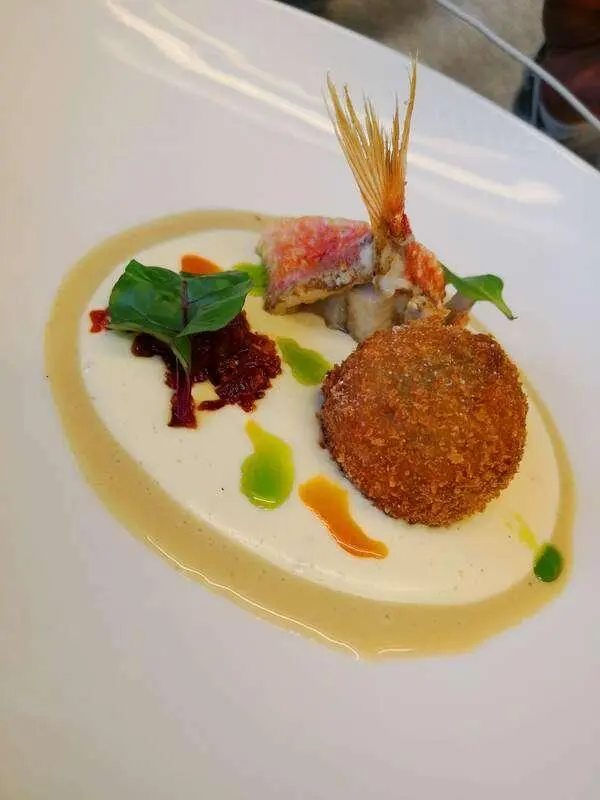 Small plated dish with a fried item, greens, sauce drizzles on a white plate