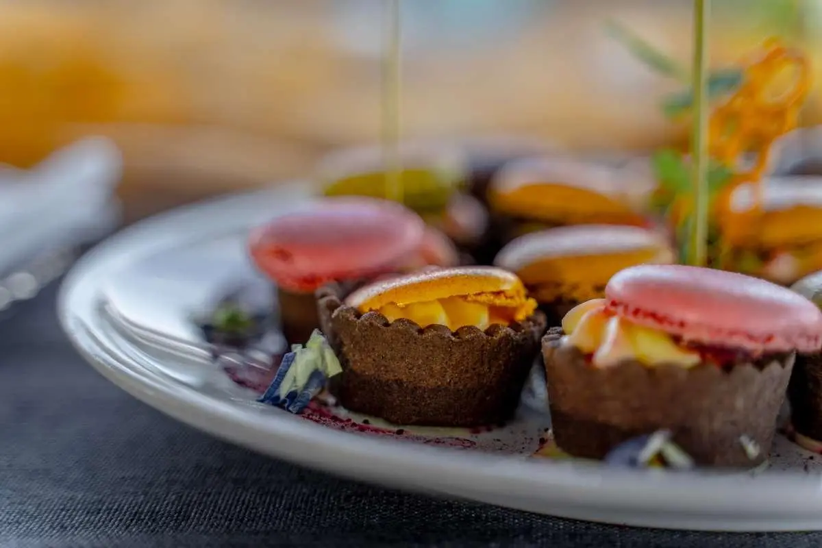 Assorted chocolate tartlets with mango cream and pink macarons on a white plate