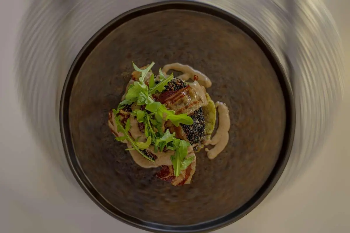 A dark round bowl with a plated appetizer, greens garnish, and meat slices