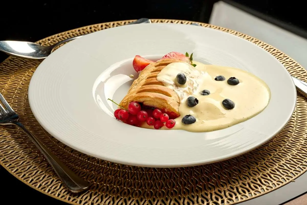 Plate with creamy dessert, raspberry sauce, blueberries, and garnishes on a white plate