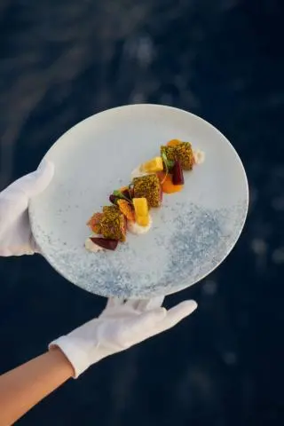 Person holding a round plate with skewered skewers over blue water
