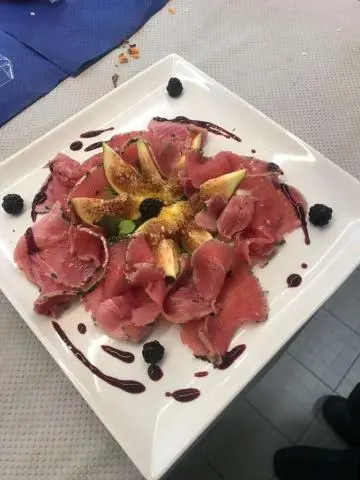 Plate with sliced red meat and sauce dots on a white square dish aboard a yacht