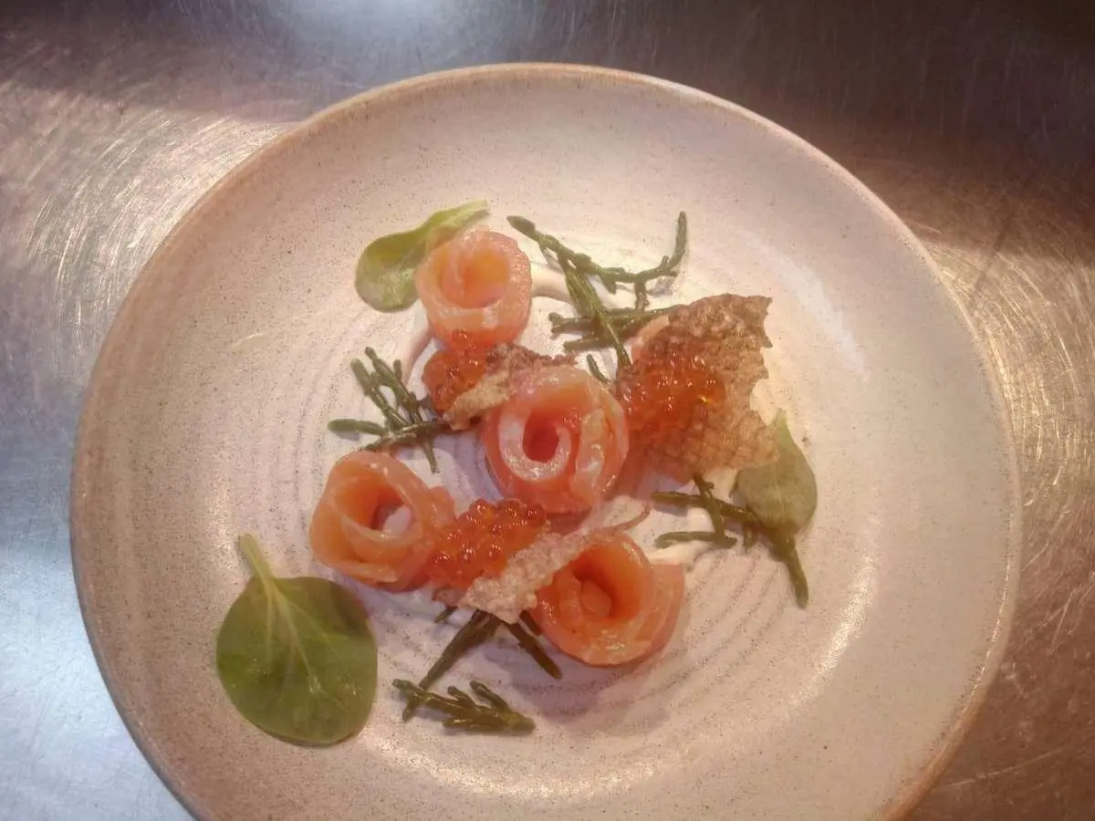 Salmon rose rolls with caviar, greens, and crispy shards on a light plate