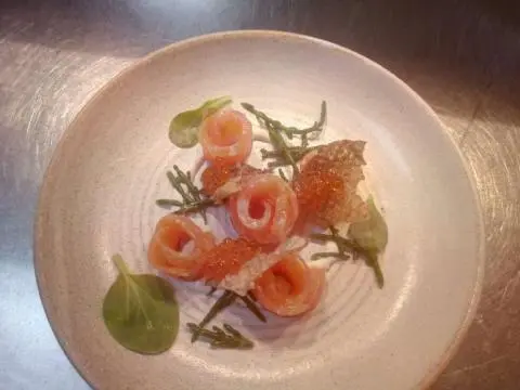 Salmon rose rolls with caviar, greens, and crispy shards on a light plate