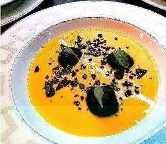 Close-up view of a bowl of bright orange soup with black olive garnish