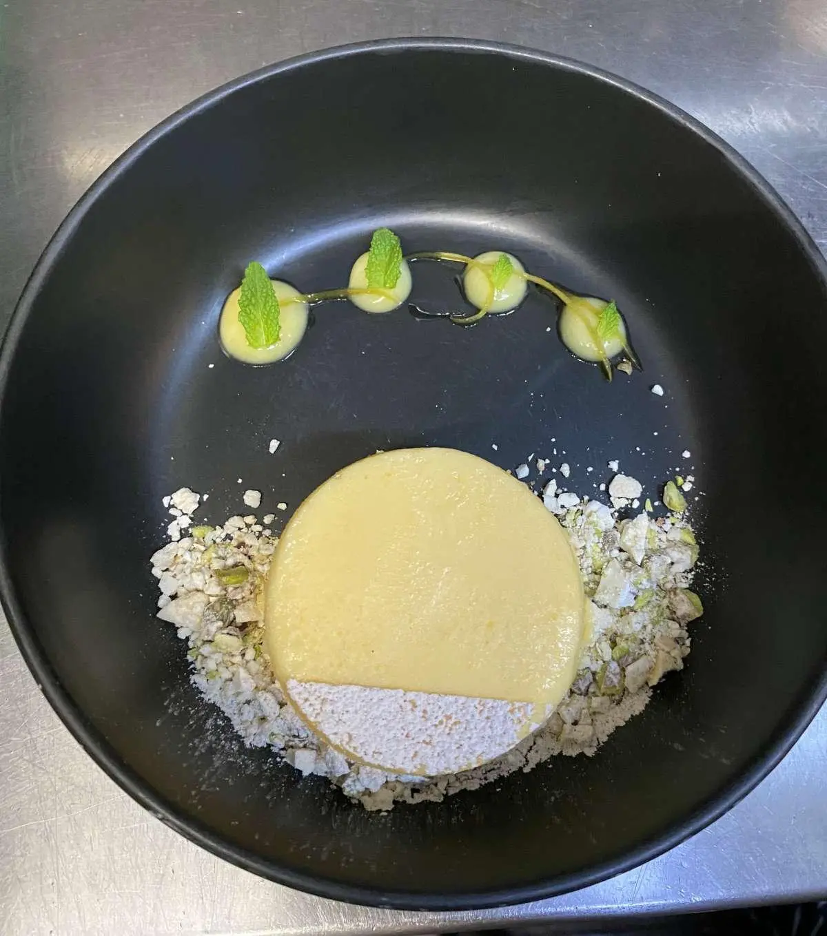 In the pan, a fried egg with sliced lime and herbs beside a round bread cracker