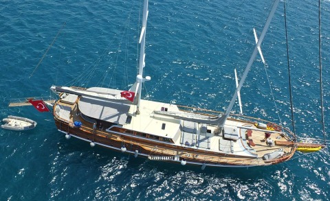 A luxury 34m yacht, Kaptan Mehmet Bugra, sails in clear blue waters with Turkish flags on deck and a small tender nearby