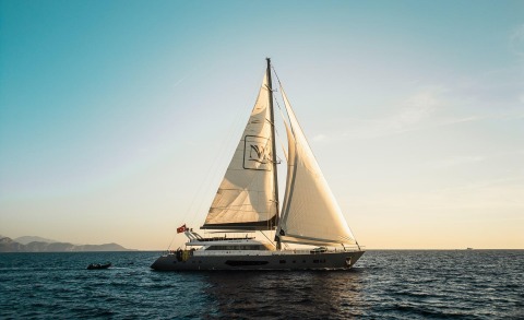 Sailing yacht on calm sea at sunset with sails raised