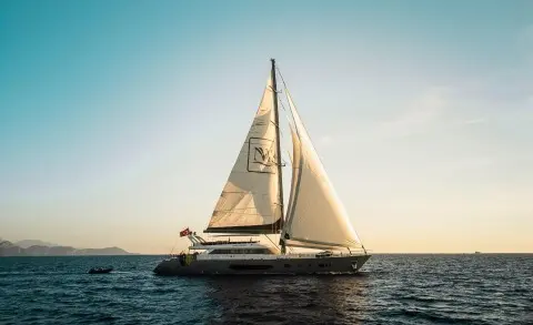Sailing yacht on calm sea at sunset with sails raised