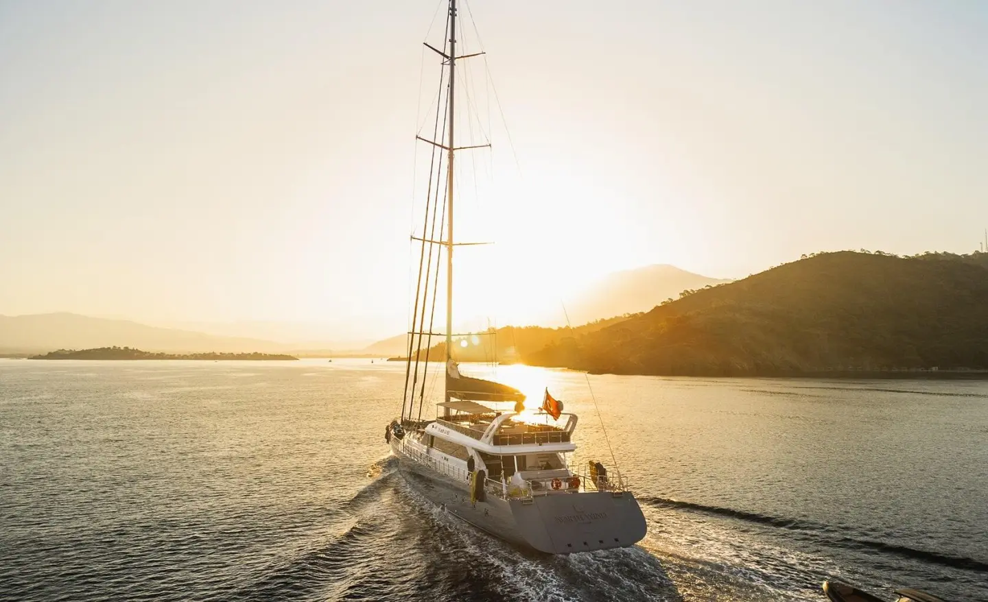 Sailing yacht on open sea at sunset with tall mast and wake behind.