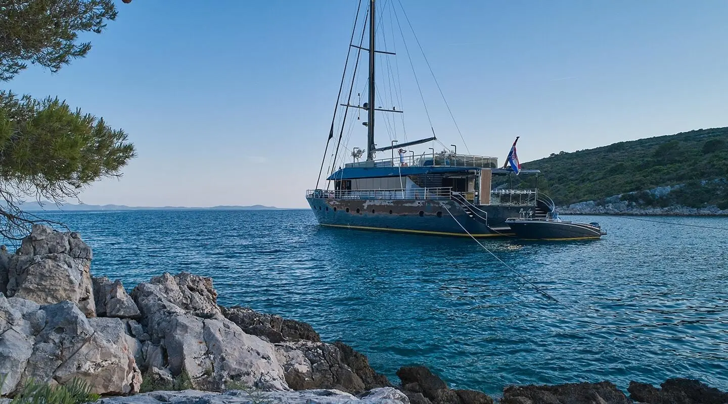 Rara Avis luxury yacht anchored near rocky coastline with clear blue water