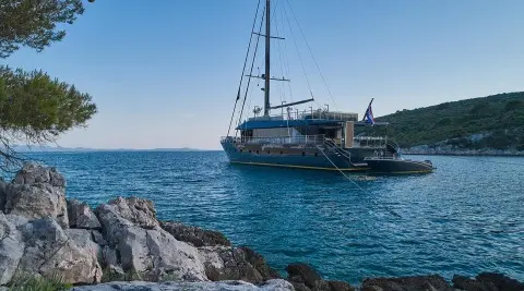 Rara Avis luxury yacht anchored near rocky coastline with clear blue water