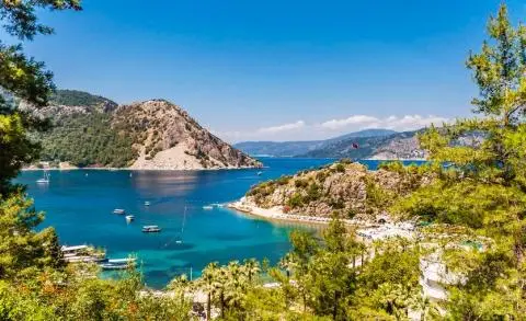 Pebble beach and hills with small boats anchored in a turquoise bay framed by trees
