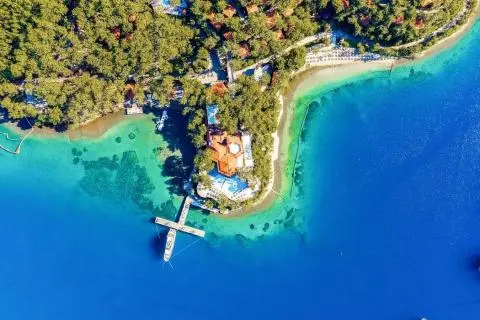 Aerial view of a yacht docked near a turquoise coastal villa and anchored over blue sea