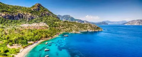 Turquoise bay with small boats along a hillside coastline and clear water