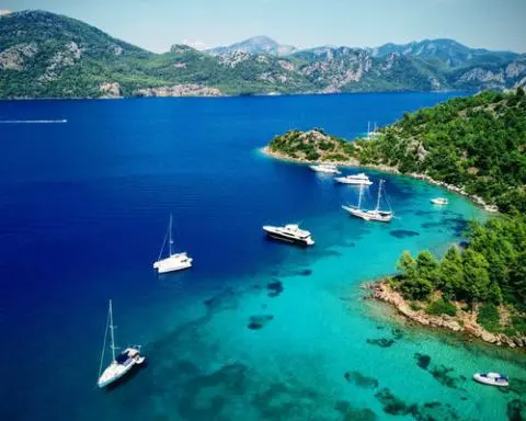 Turquoise bay with sailboats anchored near forested coastline and clear water