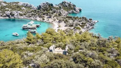 Yacht anchored in turquoise cove with rocky shoreline and greenery