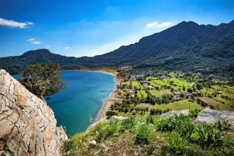 View from rocky cliff over a blue bay, curved beach and green valley with scattered houses