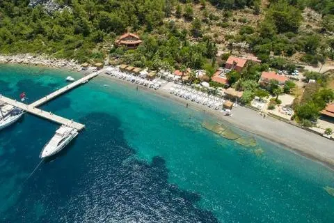 White yacht docked near turquoise water with a green shoreline and boats nearby