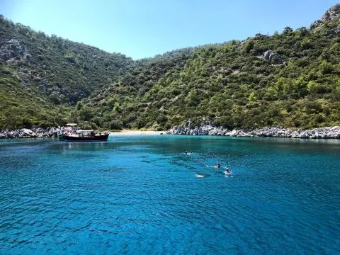 Wooden boat anchored in turquoise cove with green hills surrounding