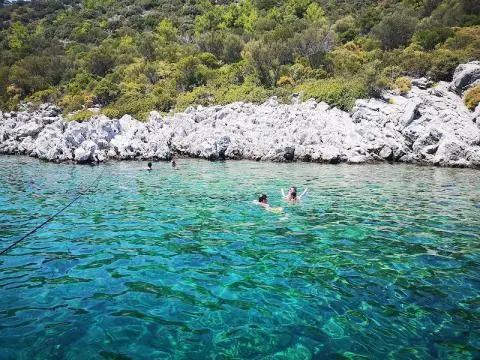 Turquoise sea near rocky shoreline with swimmers in clear water