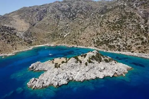 Sailboat anchored near rocky islet with turquoise water and rugged cliffs