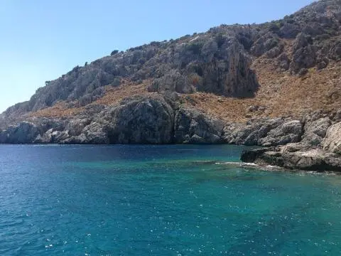 Rocky coastline with clear turquoise sea and dry, sparsely vegetated hillside