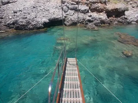 Metal gangway from yacht leading to rocky shore over clear turquoise water