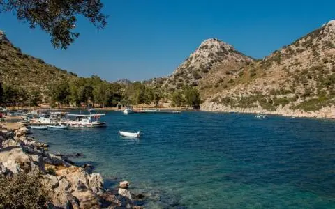 Small boats anchored near rocky coastline with clear blue waters and hills