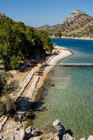 Pebble beach cove with sun loungers, straw umbrellas and clear turquoise water under trees
