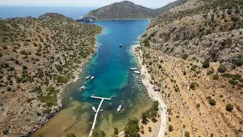 A narrow turquoise bay with a wooden pier and small boats anchored nearby