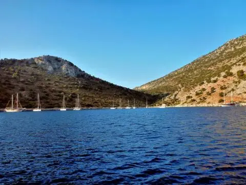 Sailboats anchored in a rocky cove with calm blue water and hills
