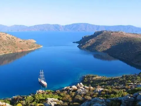 Three-masted wooden gulet anchored in a calm blue bay surrounded by rocky headlands