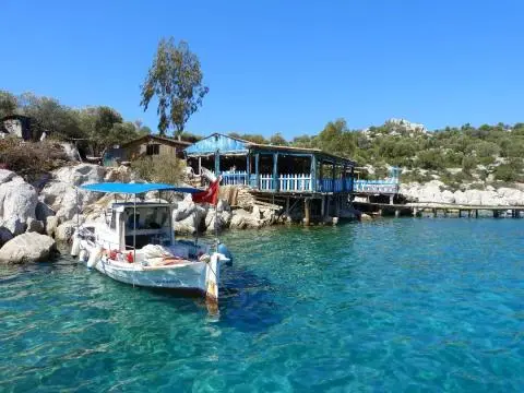 Small boat near a seaside restaurant with clear blue water and boats