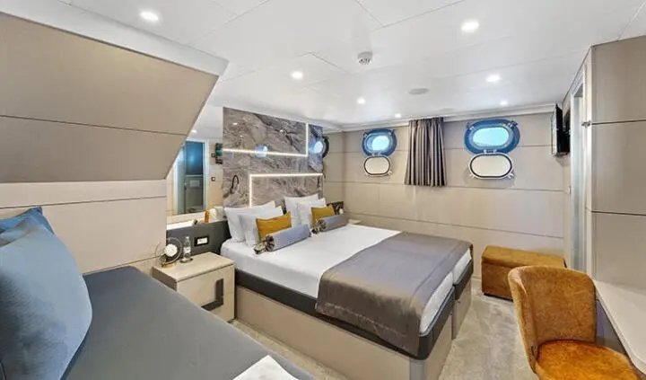Freedom yacht cabin with two twin beds, beige decor, wooden furniture, and porthole windows