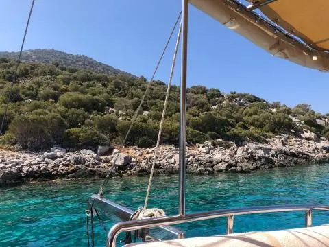 View from yacht deck toward turquoise water and rocky shoreline.