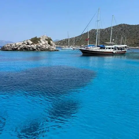 Two-masted gulet anchored in turquoise water near rocky islet under clear sky