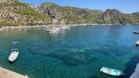 Small boats moored on clear turquoise water with a wooded rocky shoreline and docks