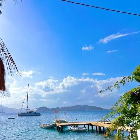 Wooden pier with small boats and a sailing catamaran docked by blue water