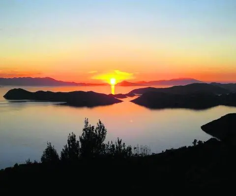 Orange sunset over islands and calm sea with the sun reflecting on the horizon