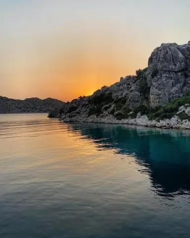 Rocky coastline with turquoise water and sunset glow reflected, steep rocks on right