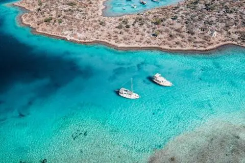 Two yachts anchored in turquoise water near rocky shoreline